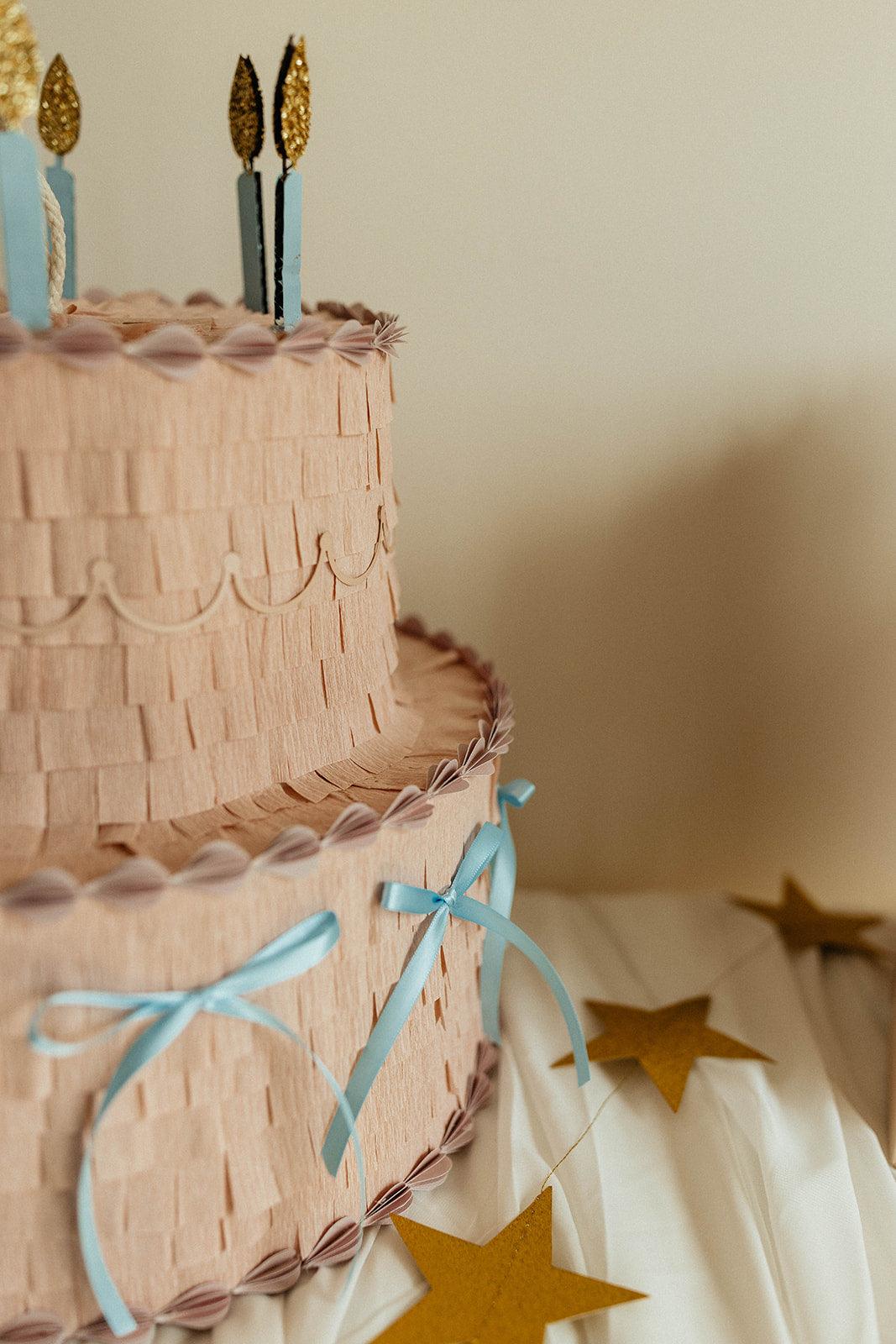 Piñata pastel rosa de dos pisos con lazos azules y estrellas doradas colgantes