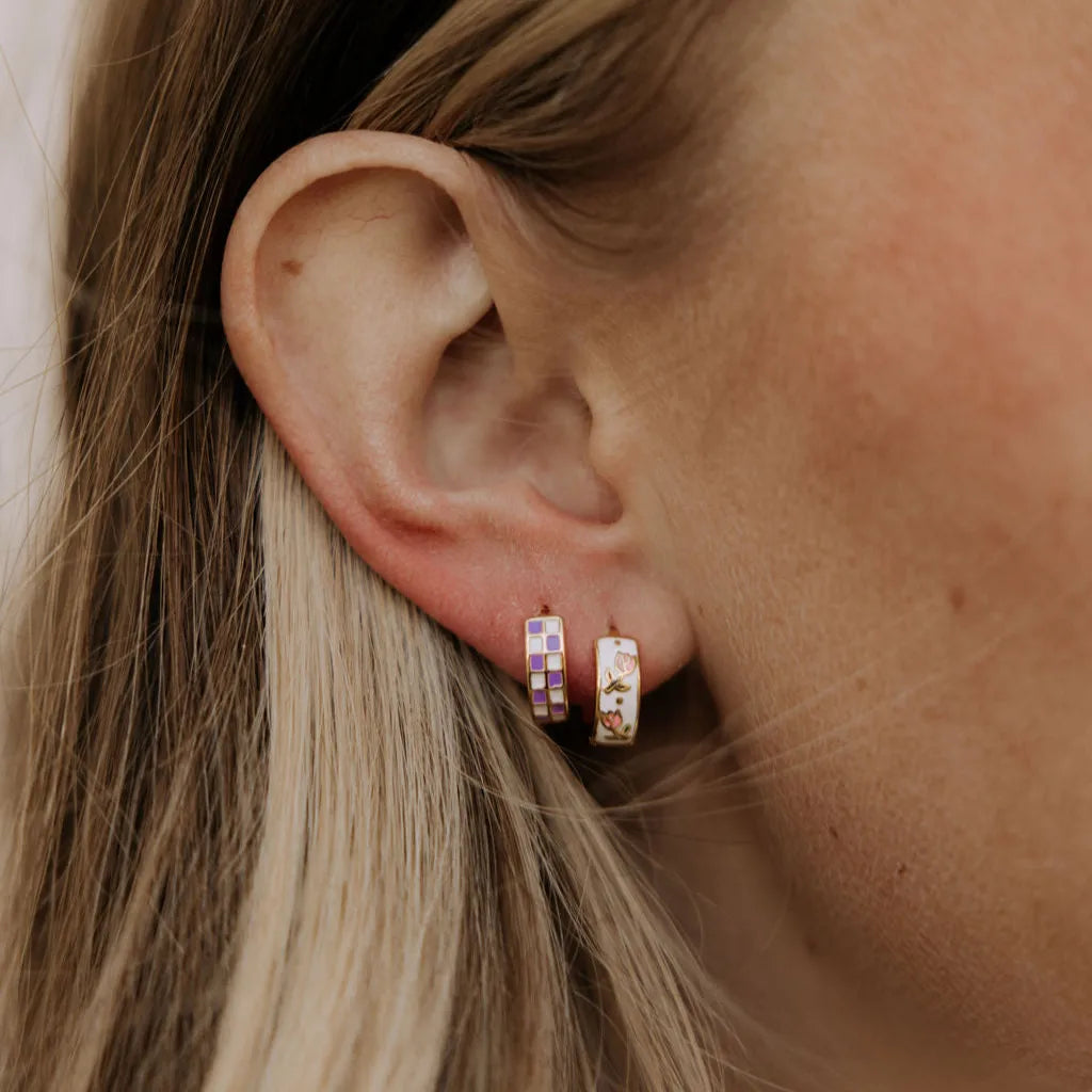 Gold-filled huggie hoop with purple and cream checkered squares worn on the ear