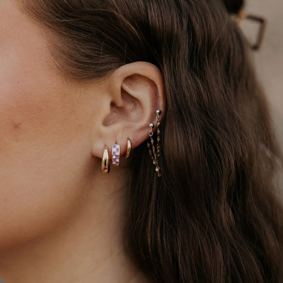 Checkered gold-filled huggie hoop earring with pastel squares worn on the ear