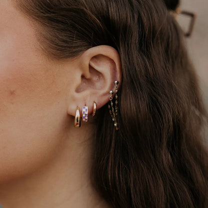 Checkered gold-filled huggie hoop earring with pastel squares worn on the ear