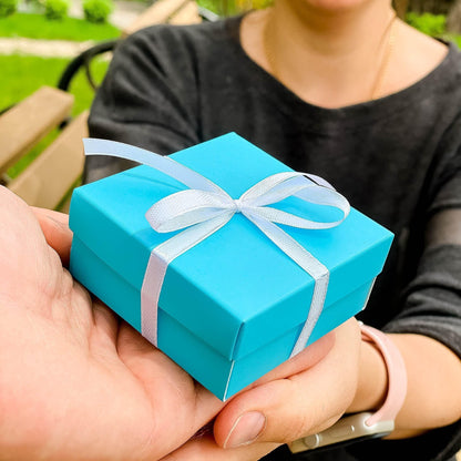 Turquoise gift box with white ribbon bow being held outdoors