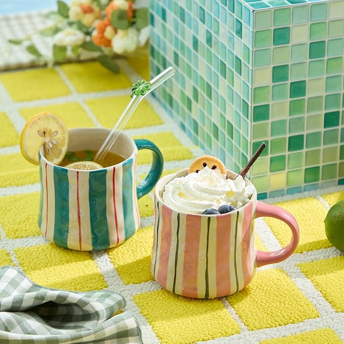 Striped ceramic mugs with curved handles, one pink and one green, on a table