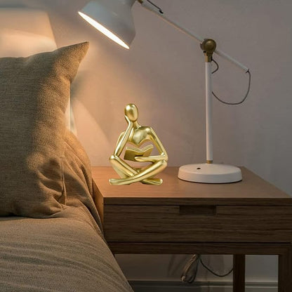 Gold resin seated thinker figurine reading a book on a bedside table