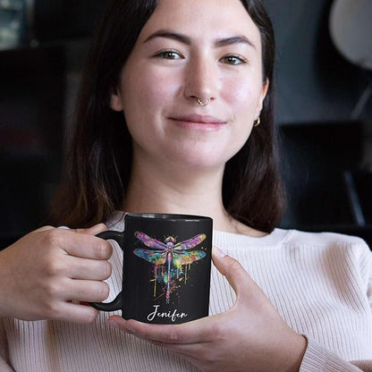 Black ceramic mug with colorful dragonfly graphic and custom name, held in hand