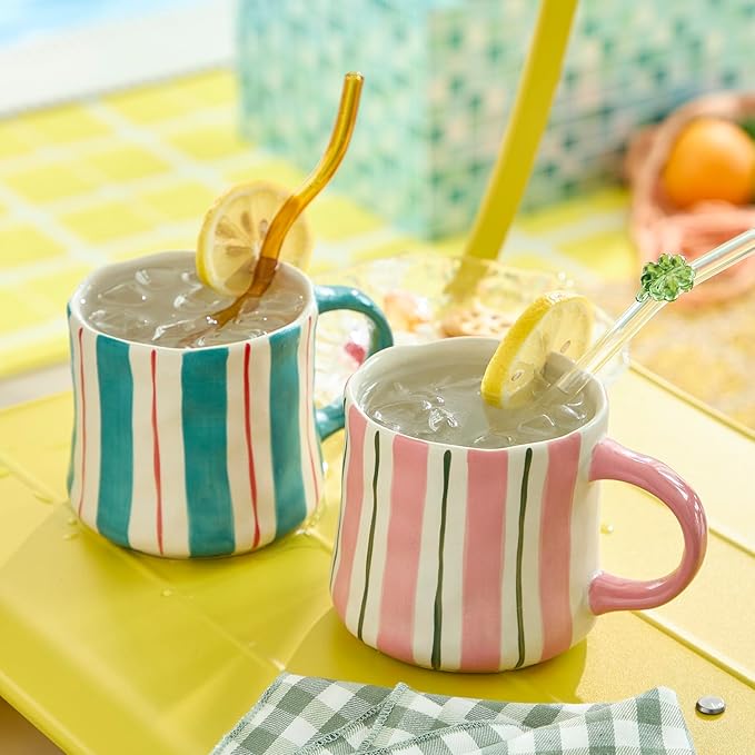 Two ceramic mugs with vertical stripes, one pink handle and one green handle