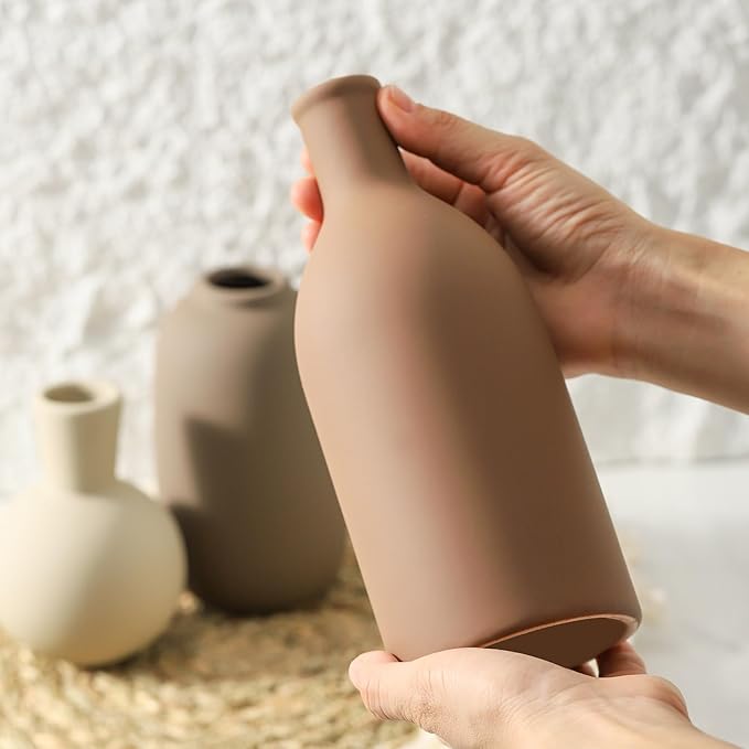 Hand holding a matte ceramic vase in terracotta brown from the set of three