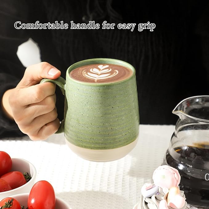 Green ceramic coffee mug with handle and latte art, held in a hand.