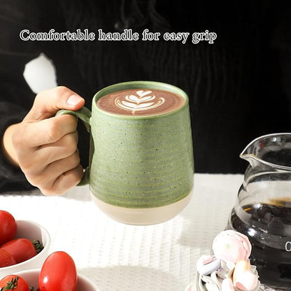 Green ceramic coffee mug with handle and latte art, held in a hand.