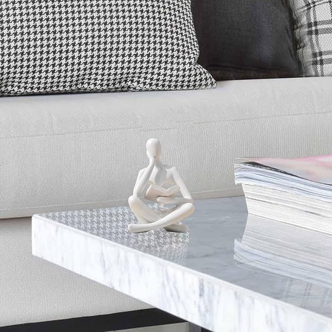 White seated reading thinker resin statue on a sofa table, holding an open book
