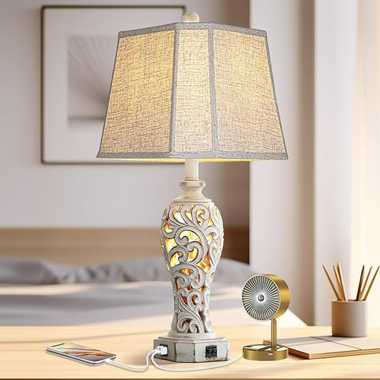 Farmhouse table lamp with beige pleated shade, carved white base, and USB charging ports.