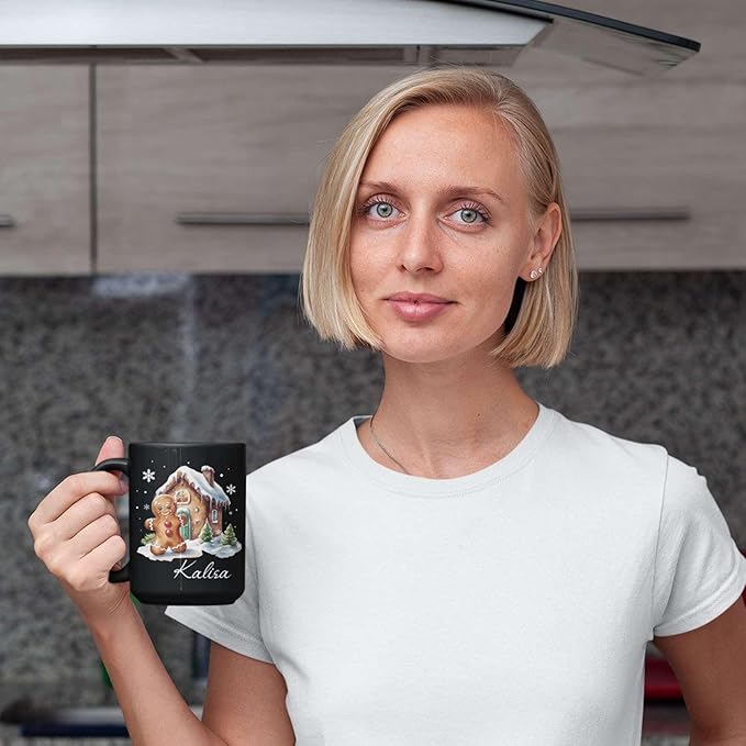 Black ceramic mug with gingerbread house graphic and “Kalisa” name, held up.