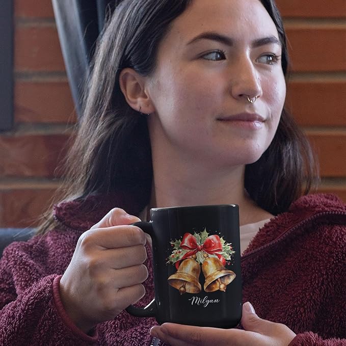 Black ceramic mug with bell and bow print and Milyan script, held near face
