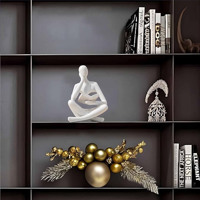 Small white seated reading thinker resin statue on a shelf, holding an open book