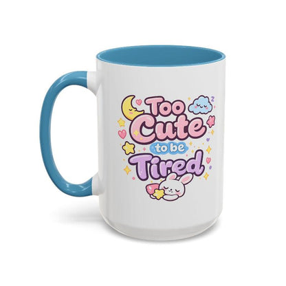 White mug with blue rim and handle, “Too Cute to be Tired” bunny graphic.