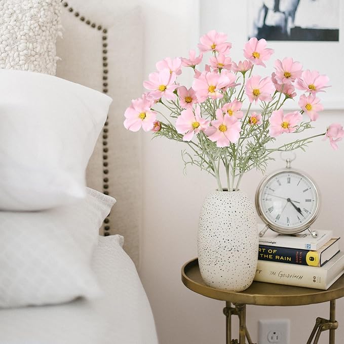 Light pink faux daisy-style flower stems in speckled white vase, with green leaves