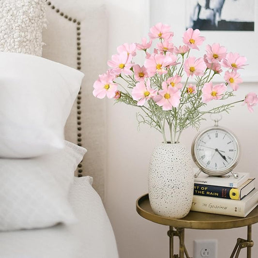 Light pink faux daisy-style flower stems in speckled white vase, with green leaves