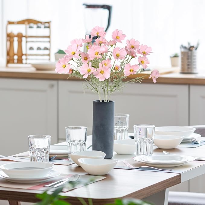 Light pink faux daisy-style flower stems in dark vase, with green leaves