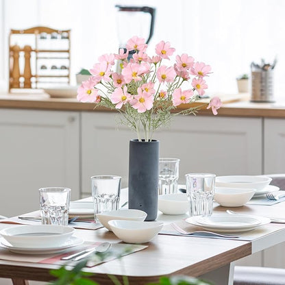 Light pink faux daisy-style flower stems in dark vase, with green leaves