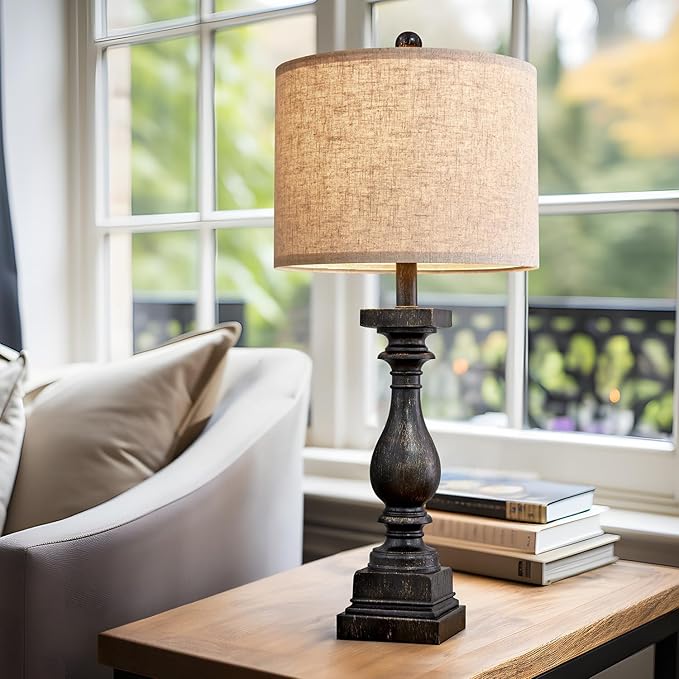Fabric-shade table lamp with dark resin pedestal base on wooden tabletop