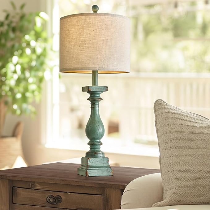 Green resin table lamp with beige shade on bedside table next to vase
