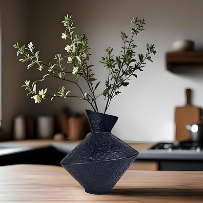 Dark hammered cast iron vase with angled neck holding green flowering stems