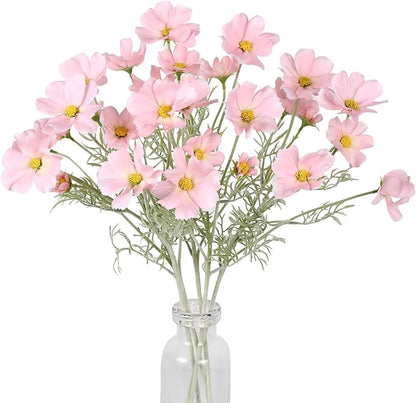 Light pink faux daisy-style flower stems with green leaves in clear vase