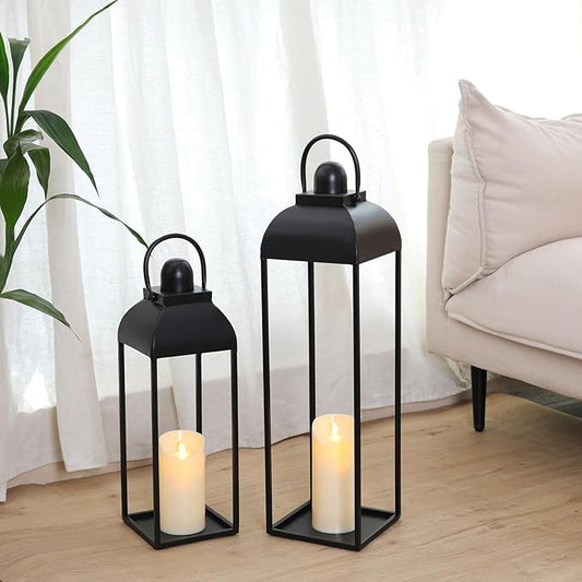 Set of 2 black metal candle lanterns with arched tops and open frames, candles lit inside.