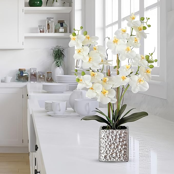 Faux white Phalaenopsis orchid arrangement in a silver textured vase on a kitchen counter