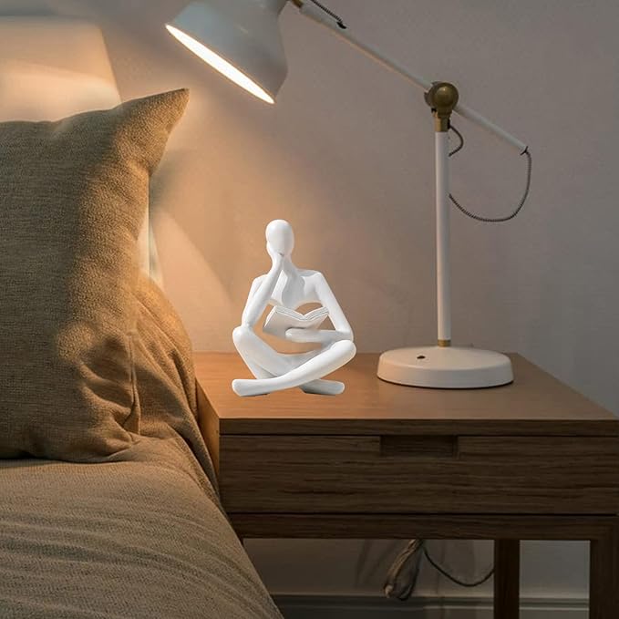 White seated reading thinker resin statue on a nightstand, holding a book