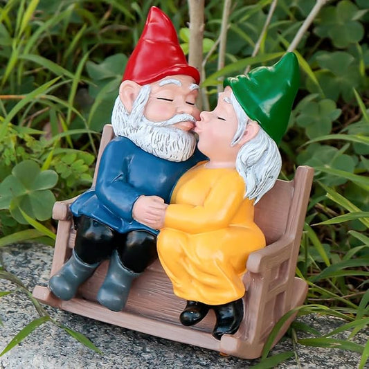 Garden gnome couple statue seated on rocking chair, leaning in to kiss, red and green hats