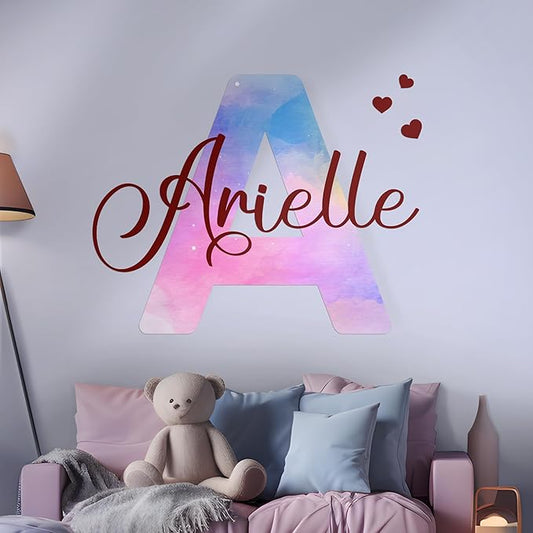 Pink and blue watercolor “Arielle” wall decal with hearts on nursery wall above teddy bear.