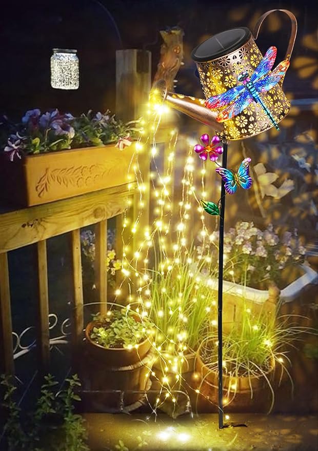 Solar watering can stake light with dragonfly decor, bright warm yellow glow near plants