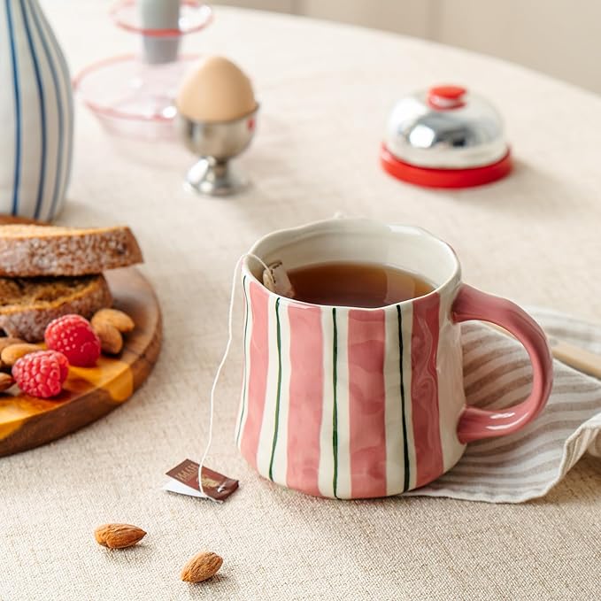Striped ceramic mug with pink handle and vertical green lines, holding a cup of coffee