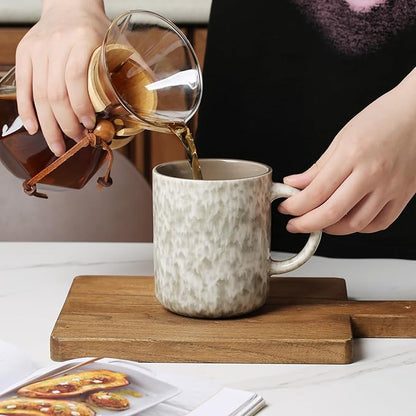 Speckled ceramic mug with curved handle as tea is poured from a glass kettle