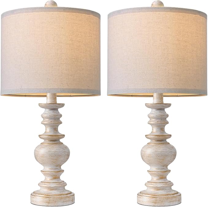 Close-up of two farmhouse table lamps with beige linen shades and whitewashed bases
