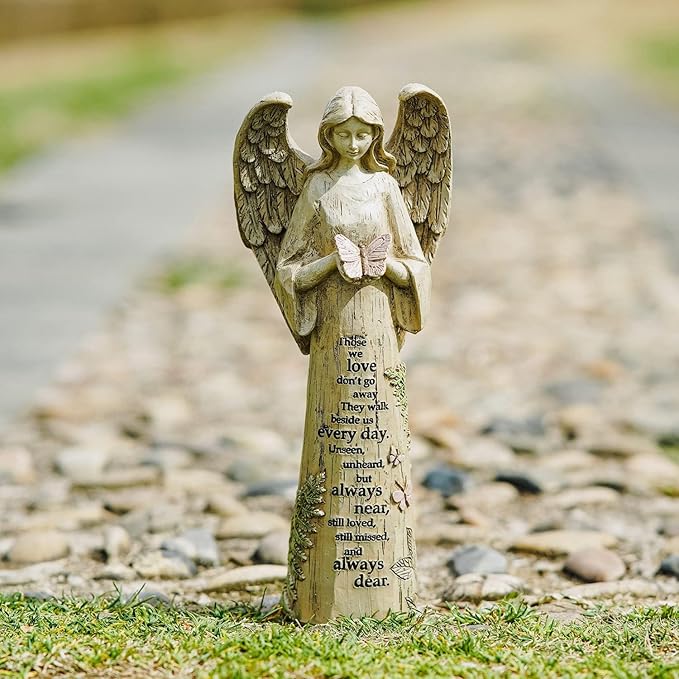 Garden angel statue with a pink butterfly, floral accents, and a memorial message.