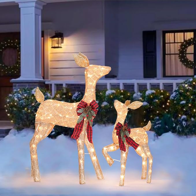Two illuminated golden reindeer decorations with red plaid bows on snowy outdoor display