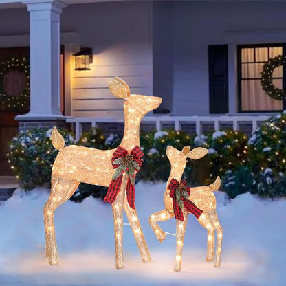 Two illuminated golden reindeer decorations with red plaid bows on snowy outdoor display