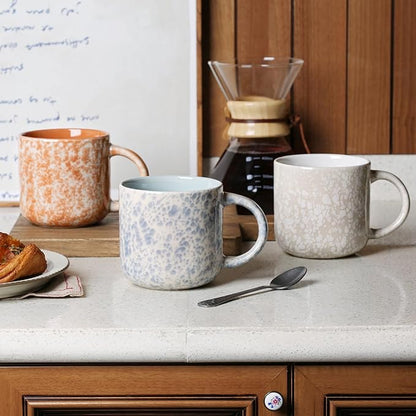 Set of ceramic coffee mugs with handles on a tabletop, including speckled blue and white