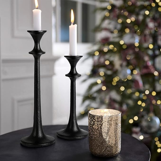 Black iron taper candle holders holding lit white tapers, staggered height pair