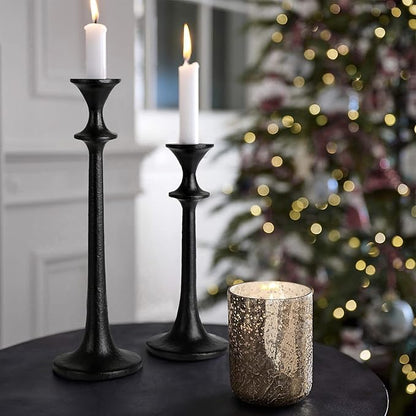 Black iron taper candle holders holding lit white tapers, staggered height pair