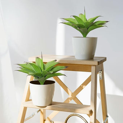 Two dark green faux agave plants in white pots on a wooden stand