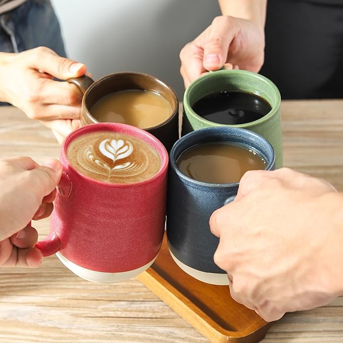 Hands holding four ceramic coffee mugs with latte art in red, brown, green, and blue.
