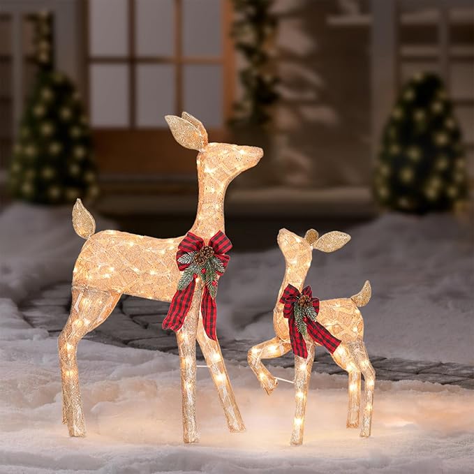 Two lit golden reindeer decorations with red plaid bows on snow-covered ground
