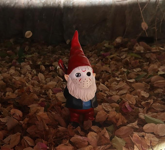 Small red-hat gnome outdoor statue with white beard and blue outfit on leaves
