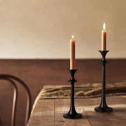 Two black iron taper candle holders with lit candles, standing on a wooden surface