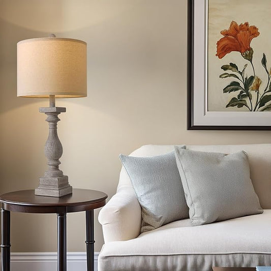 Antique gray pedestal table lamp with beige drum shade on a side table