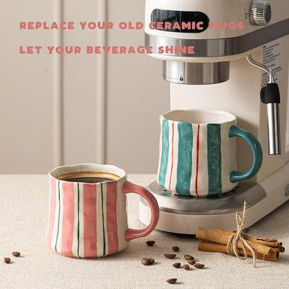 Two striped ceramic mugs with pink handles and green vertical lines on a countertop
