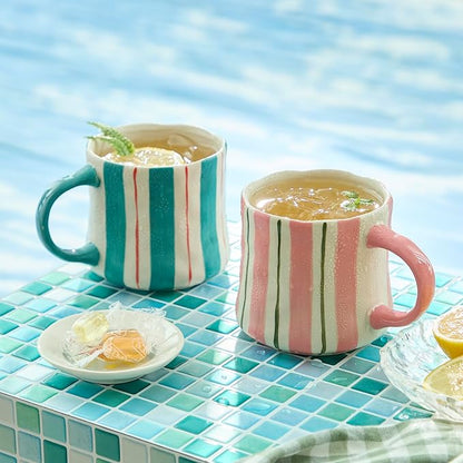 Two striped ceramic mugs on a turquoise tiled surface: pink and teal-green designs
