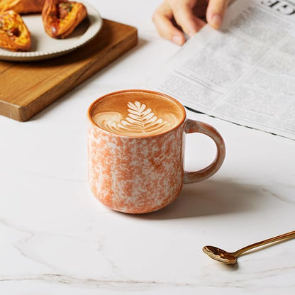 Speckled ceramic coffee mug with handle, orange exterior with latte art on top